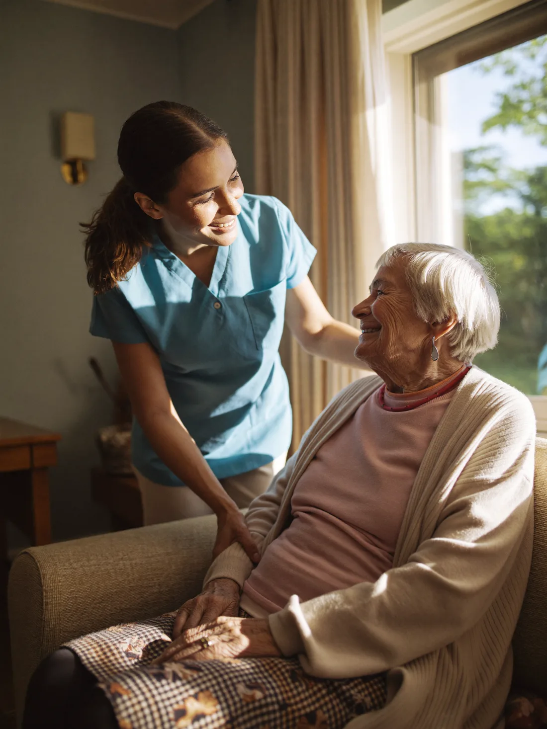 Betreuungskraft und Seniorin im Gespräch in einem hellen Wohnzimmer